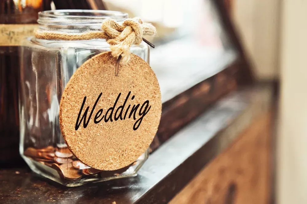 Tarro de cristal con monedas y una etiqueta de corcho con la palabra Wedding (imagen ilustrativa)
