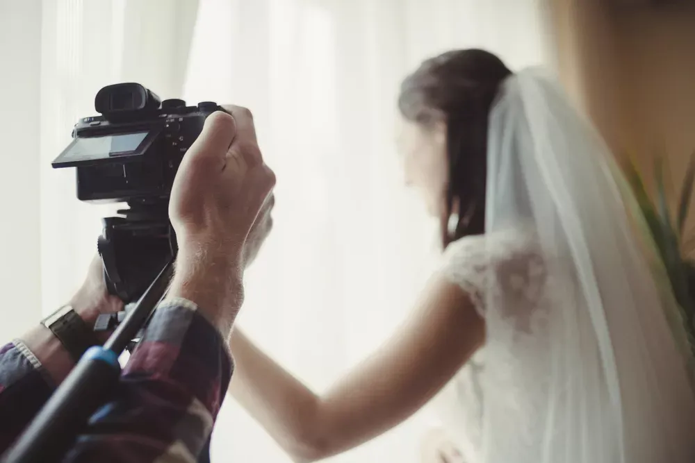 Videógrafo grabando a una novia con velo junto a una ventana con luz natural (imagen ilustrativa)
